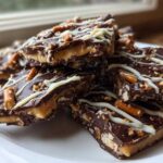 A stack of rich peanut butter pretzel bark pieces topped with dark chocolate and white chocolate drizzle.