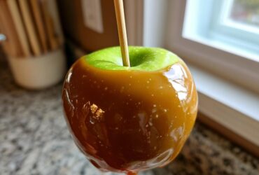 Close-up of a shiny, homemade caramel apples dipped over a bright green Granny Smith apple with a wooden stick inserted.