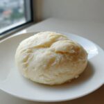 A smooth, round serving of homemade fufu resting on a clean white plate, ready to eat.