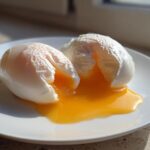 Two perfectly poached eggs, cut open to reveal bright orange, runny yolks spilling onto a white plate.