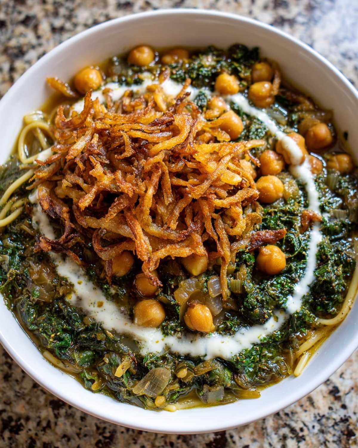 Overhead close-up of a bowl of rich persian noodle soup topped with fried onions, chickpeas, and a drizzle of yogurt sauce.