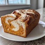 A freshly baked loaf of pumpkin cream cheese bread showing a beautiful orange and white swirl pattern inside.