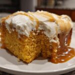 A moist slice of orange pumpkin poke cake topped with white frosting and drizzled with caramel sauce.