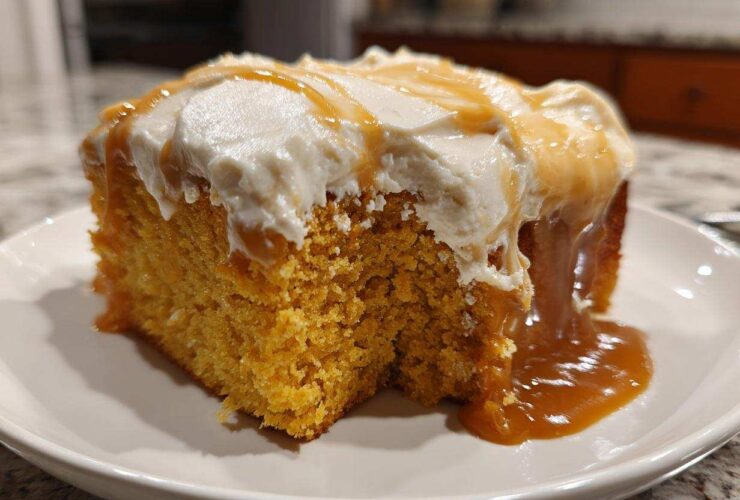 A moist slice of orange pumpkin poke cake topped with white frosting and drizzled with caramel sauce.