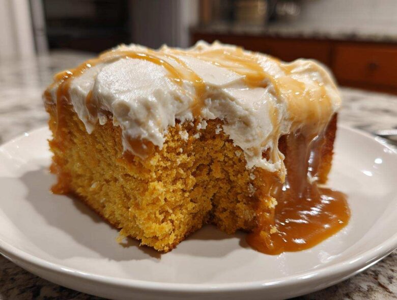 A moist slice of orange pumpkin poke cake topped with white frosting and drizzled with caramel sauce.