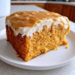 Close-up of a moist slice of pumpkin poke cake topped with cream cheese frosting and drizzled caramel sauce.