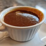 Close-up of rich, dark homemade brown gravy served in a small, white, handled ramekin on a matching saucer.