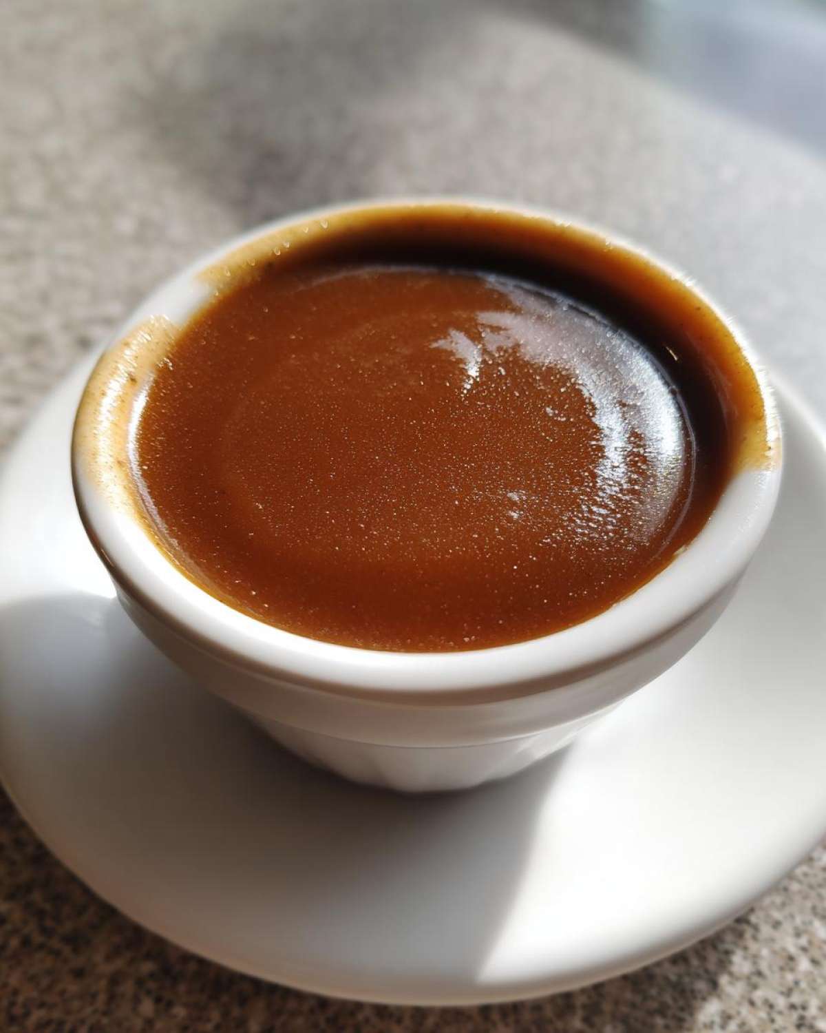 Close-up of rich, glossy homemade brown gravy served in a small white ramekin on a saucer.