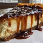 A decadent slice of salted caramel cheesecake with thick caramel sauce dripping down the sides and sprinkled with sea salt.