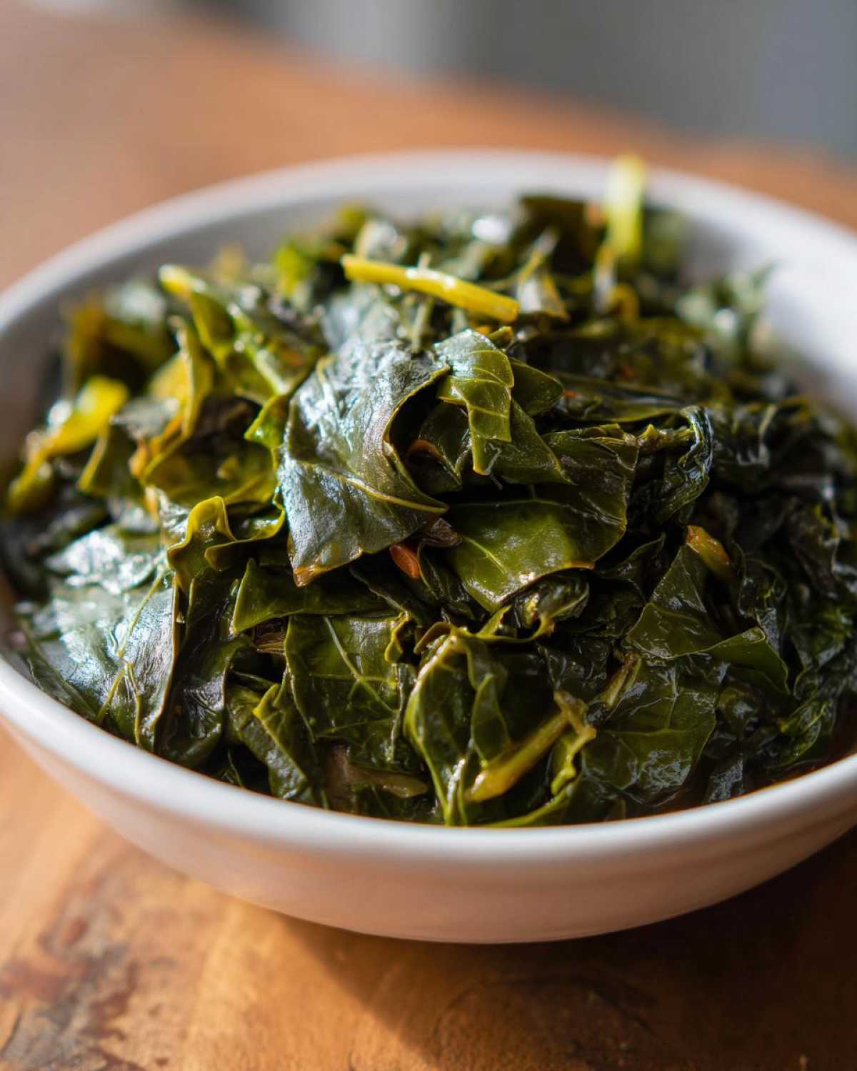Close-up of tender, dark green collard greens served hot in a white bowl.