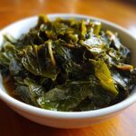 Close-up of tender, dark green collard greens simmering in savory pot liquor in a white bowl.
