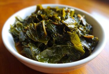 Close-up of tender, dark green collard greens simmering in savory pot liquor in a white bowl.