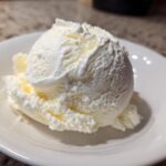 A perfect scoop of creamy, white cottage cheese ice cream served in a small white bowl.