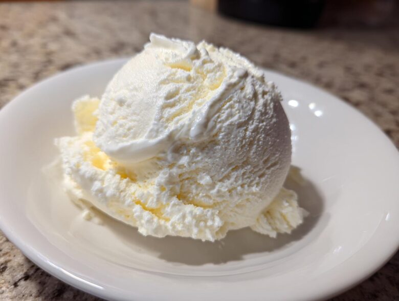 A perfect scoop of creamy, white cottage cheese ice cream served in a small white bowl.