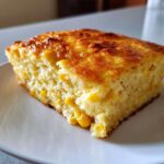 A square slice of moist cream cheese corn casserole with visible whole corn kernels and a golden-brown top.