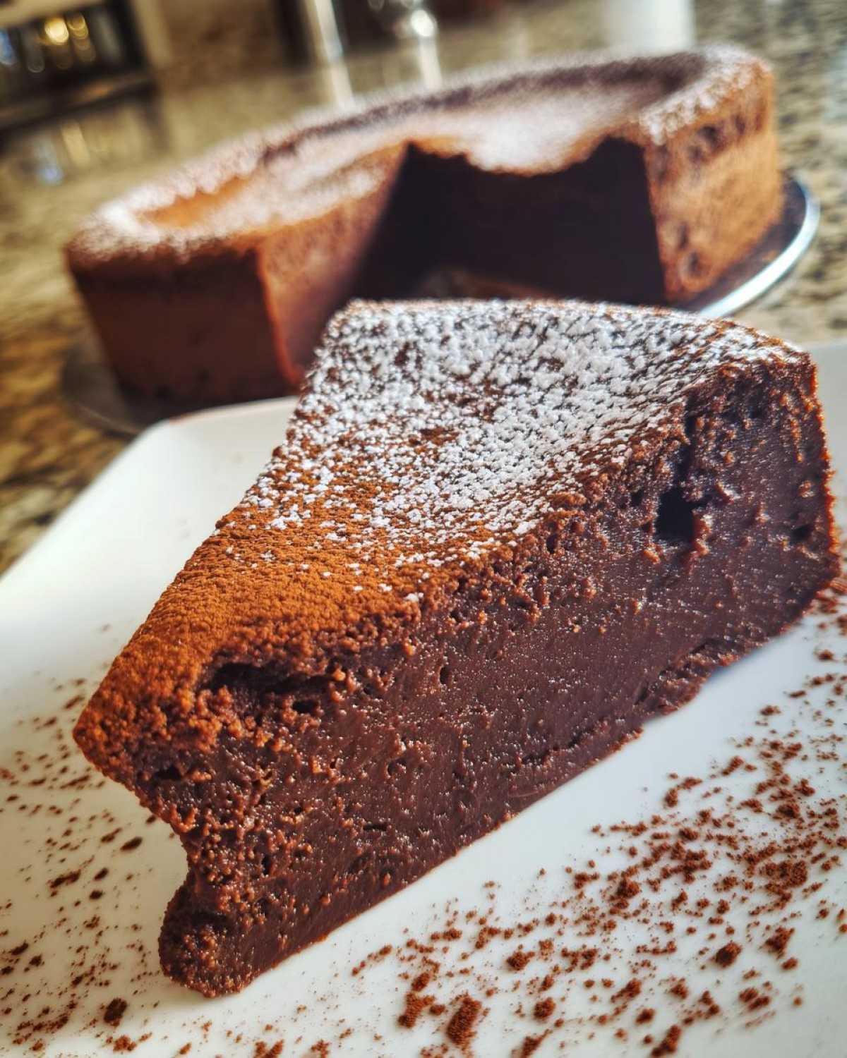 A decadent slice of flourless chocolate torte dusted with powdered sugar on a white plate.