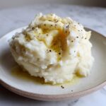 A generous serving of creamy slow cooker mashed potatoes topped with melted butter and cracked black pepper.