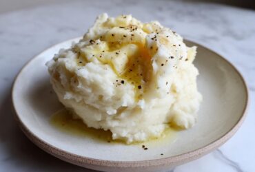 A generous serving of creamy slow cooker mashed potatoes topped with melted butter and cracked black pepper.
