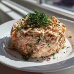 A mound of creamy smoked salmon dip, garnished generously with fresh dill and spices, sitting on a white plate.
