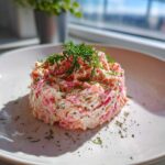 A perfectly molded serving of creamy smoked salmon dip, garnished heavily with fresh dill and cracked black pepper.