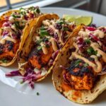 Three delicious salmon tacos filled with blackened salmon, purple cabbage slaw, and drizzled with spicy sauce.