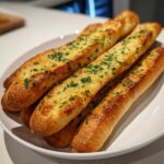 A pile of golden, soft garlic breadsticks brushed with butter and sprinkled generously with fresh green parsley.