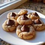 A pile of freshly baked, sugar-coated peanut butter kiss cookies topped with melted chocolate kisses.
