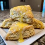 A stack of four freshly baked lemon scones generously drizzled with a thick, bright yellow lemon glaze.