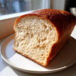 A close-up of a freshly baked sourdough sandwich bread loaf, showing a soft, open crumb structure and golden crust.