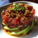 A vibrant mound of spicy tuna tartare served over fanned avocado slices, garnished with green onions.