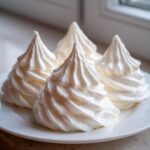 Four peaks of stiff, white royal icing, perfect for gingerbread house icing, piped onto a white plate.