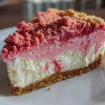 Close-up of a slice of strawberry crunch cheesecake showing distinct layers and pink crumble topping.