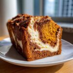 Close-up of a moist slice of pumpkin cream cheese bread showing rich orange pumpkin batter swirled with white cream cheese filling.