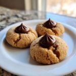 Three soft peanut butter blossom cookies rolled in sugar, each topped with a swirl of chocolate frosting, resting on a white plate.