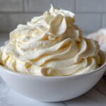 A generous swirl of light yellow vanilla buttercream frosting piped high in a white bowl.