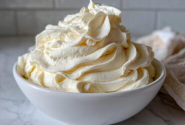 A generous swirl of light yellow vanilla buttercream frosting piped high in a white bowl.