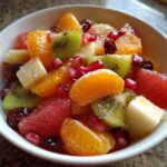 Close-up of a vibrant winter fruit salad featuring kiwi, orange segments, grapefruit, and pomegranate seeds in a white bowl.