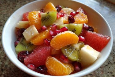 Close-up of a vibrant winter fruit salad featuring kiwi, orange segments, grapefruit, and pomegranate seeds in a white bowl.