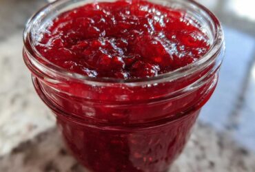 Close-up of vibrant, glistening homemade raspberry jam filling a glass jar.