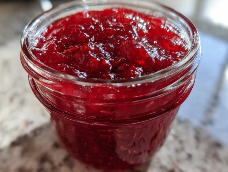 Close-up of vibrant, glistening homemade raspberry jam filling a glass jar.