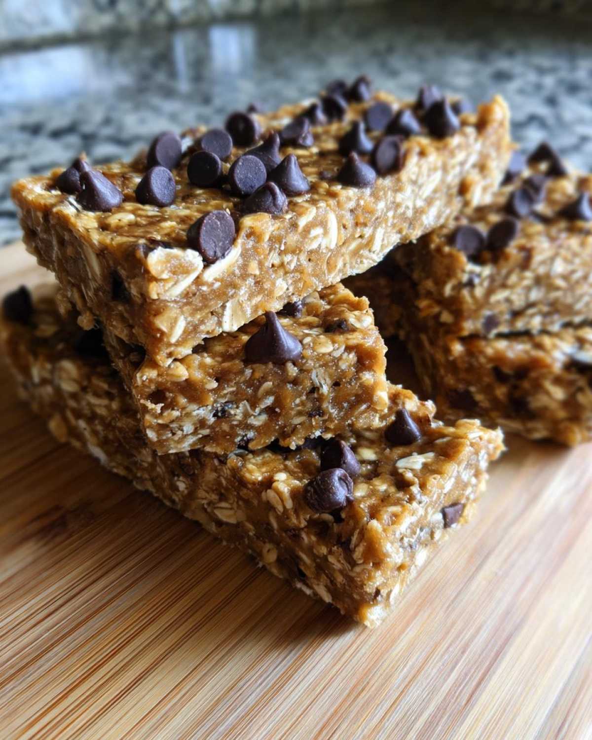 Stack of homemade chocolate chip protein bars made with oats, sitting on a wooden cutting board.