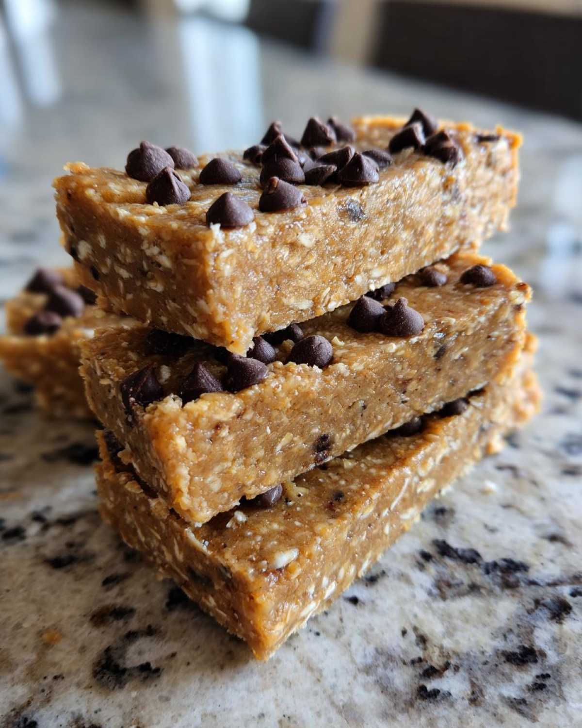 A close-up stack of three homemade, no-bake protein bars topped with mini chocolate chips.