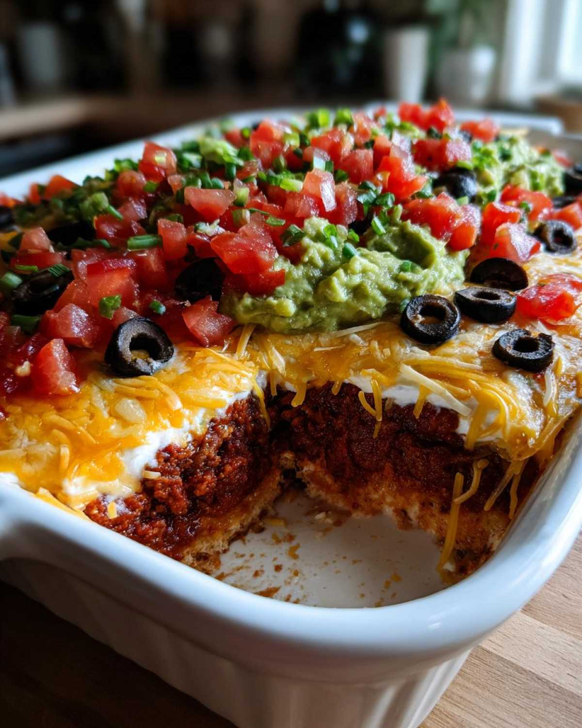 A serving dish showing a cross-section of the amazing 7 layer dip with visible layers of meat, sour cream, cheese, guacamole, tomatoes, and olives.