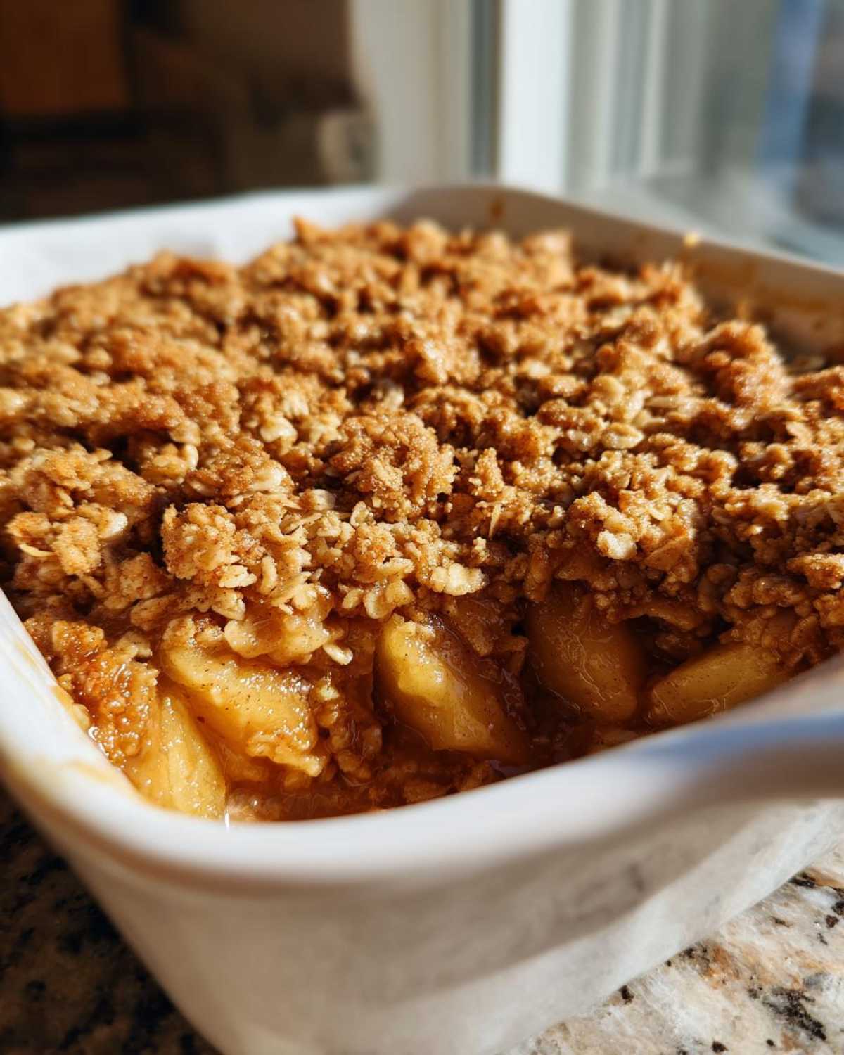 Close-up of a bubbling apple crisp recipe with a golden brown oat topping in a white baking dish.
