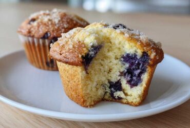 Close-up of a freshly baked blueberry muffin cut in half showing moist interior and large blueberries, part of a batch of blueberry muffins.