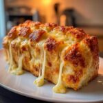 Close-up of a freshly baked loaf of cheese bread with gooey, melted cheese dripping down the sides.