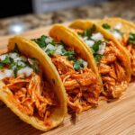 Four crispy shell chicken tacos filled with shredded orange chicken, topped with diced white onion and fresh cilantro.