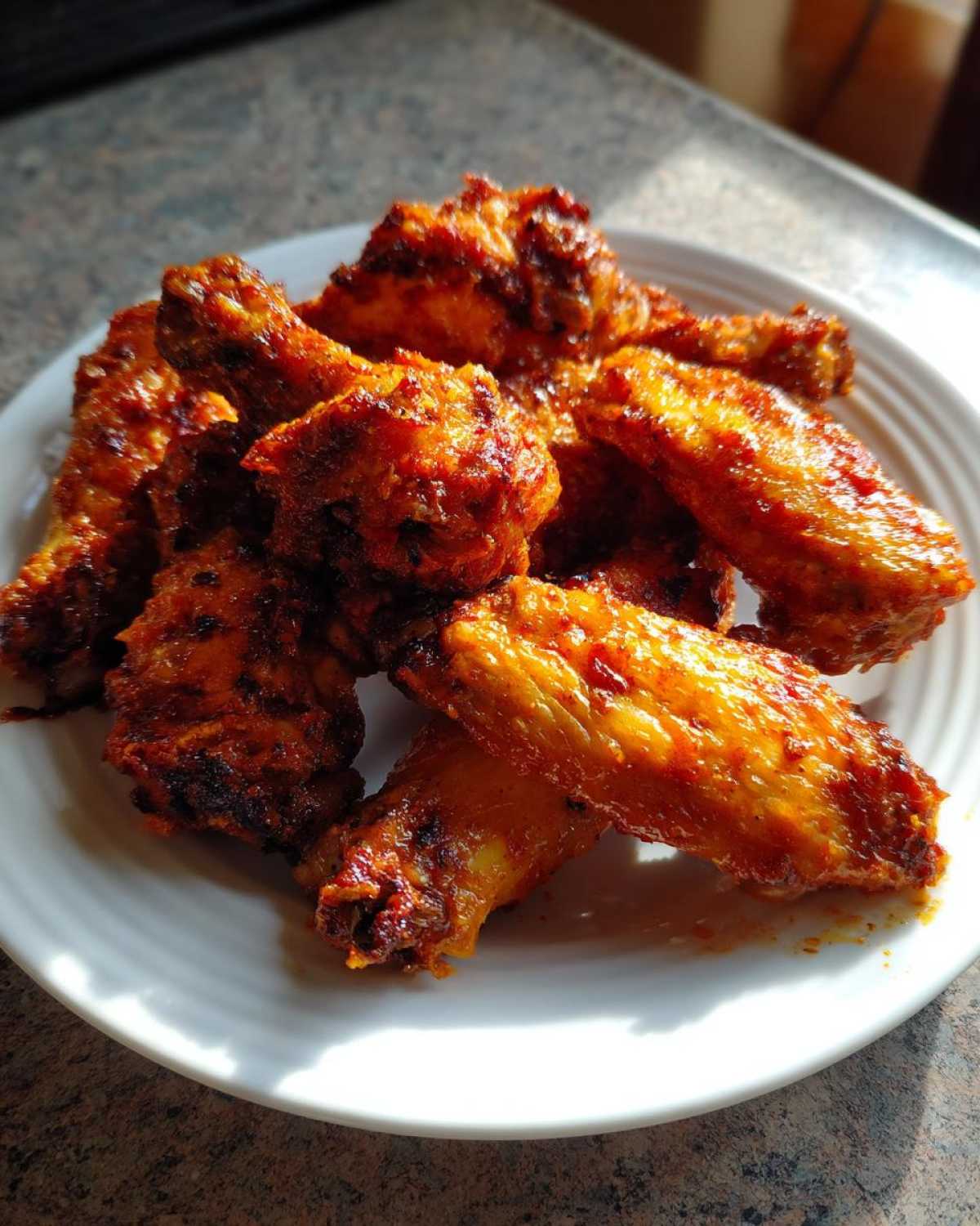 A close-up of several crispy, glazed chicken wings piled on a white plate.