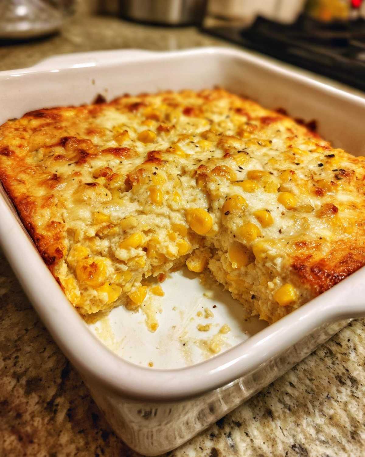 A baked portion of amazing corn dip with cream cheese, showing a golden-brown top layer and creamy texture inside a white baking dish.