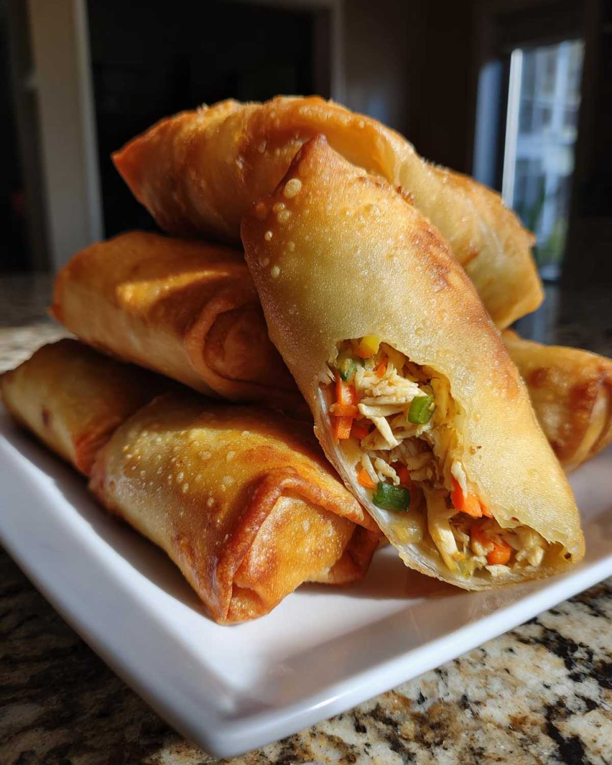 A stack of golden brown, crispy fried egg roll appetizers, with one cut open showing the shredded chicken and vegetable filling.